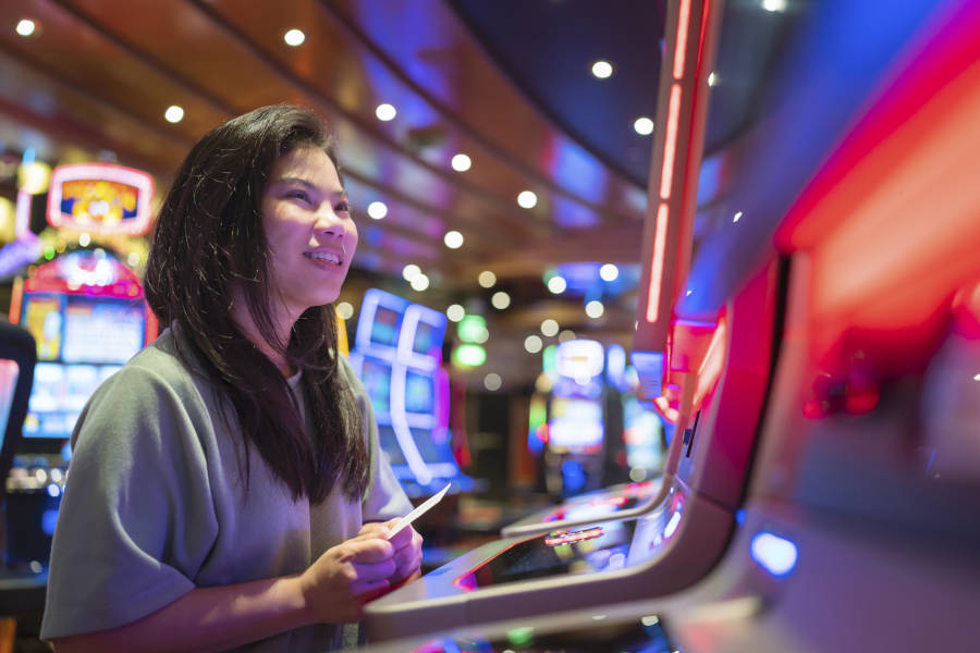 Women playing a slot machine at a Casino with money in hand.